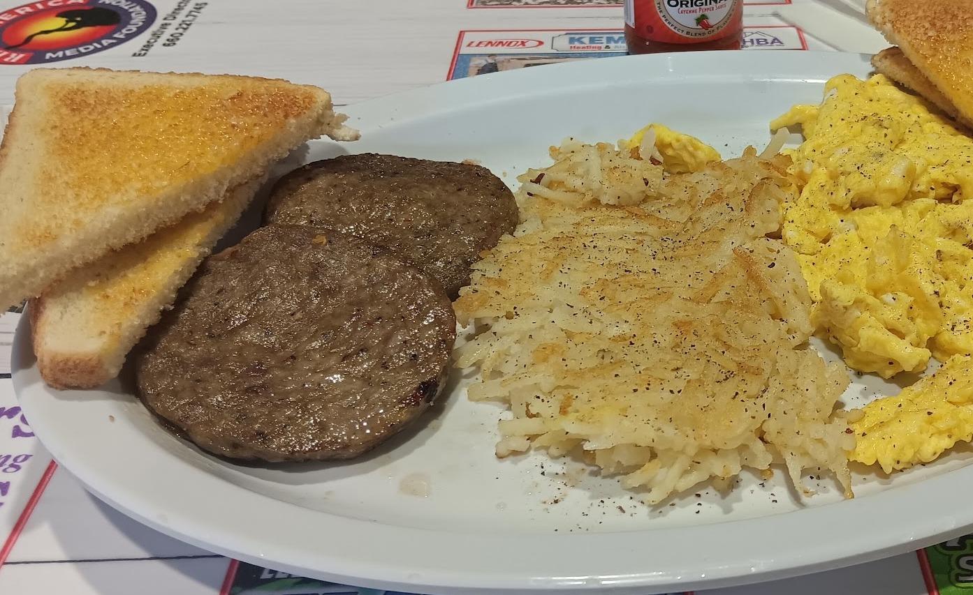 Sausage patties, hash browns, scrambled eggs and buttered toast on a white oval plate.